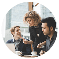 Three people smiling while having a discussion in front of laptop
