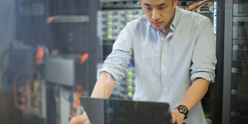 Young IT worker looking at laptop in server room