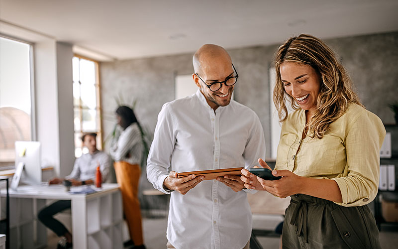 Two office colleagues gathered on devices in office