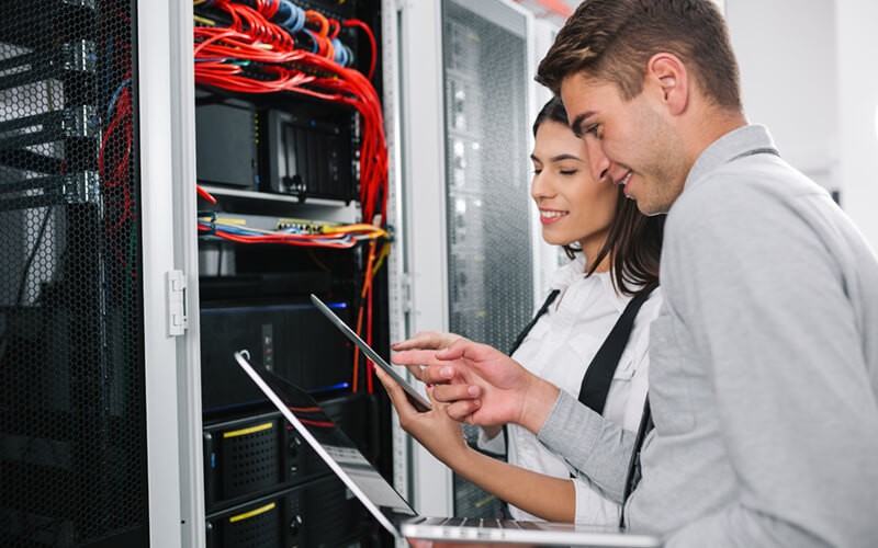 Next-generation technology that lowers risk while increasing performance Two IT engineers on-site in data center with laptop