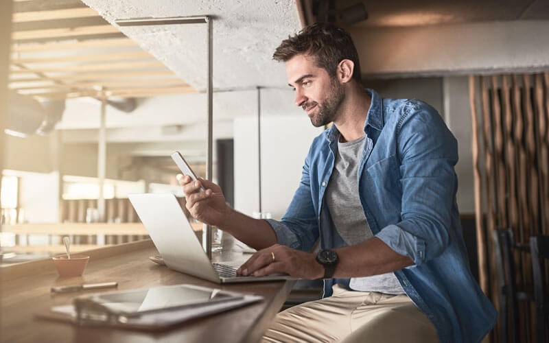 Man on mobile device in front of laptop computer