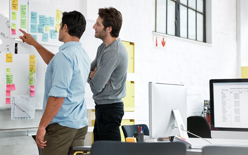 Determine an action plan Two designers collaborating in office with sticky notes on whiteboard