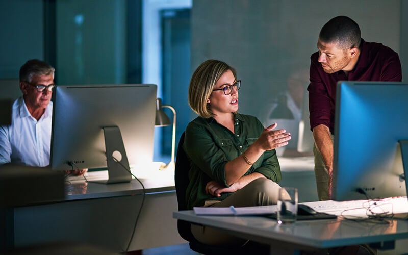 We'll design a holistic solution Colleagues analyzing data on computer in office at night