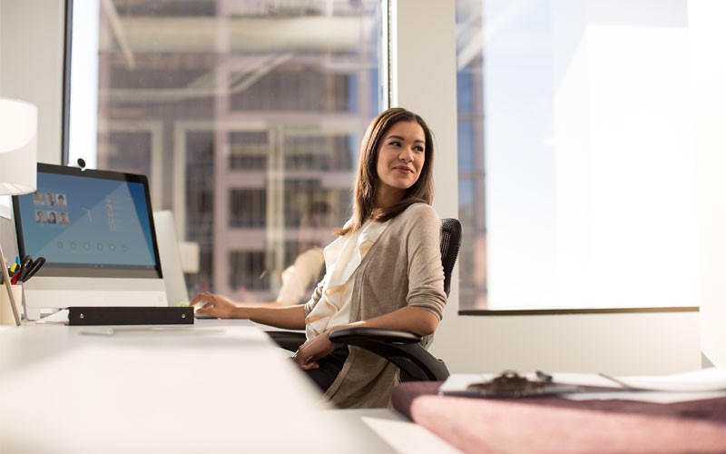 Evolve your digital network with software solutions that drive your business outcome Young woman at desk with laptop reclining in her chair.