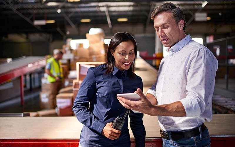 Manage your mobile workforce with ease. Two business colleagues use mobile tablet device