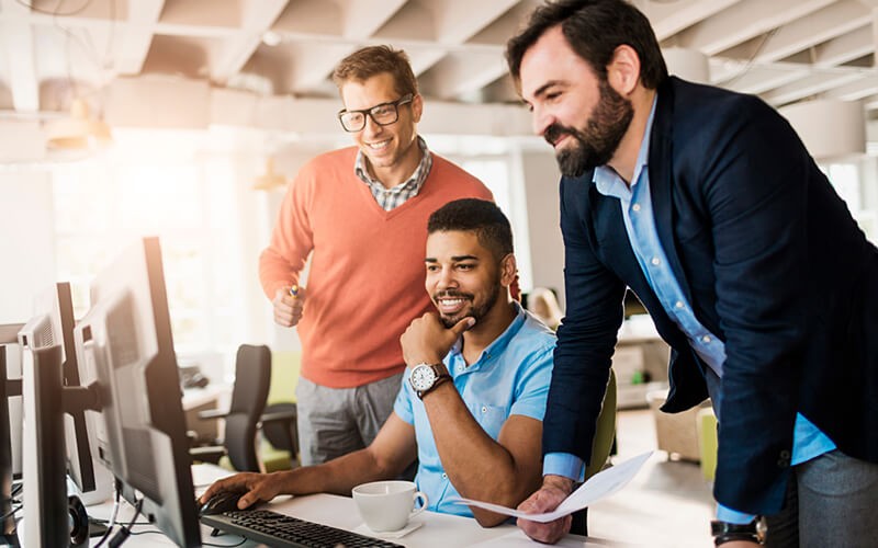 Three business colleagues gather around desktop computer