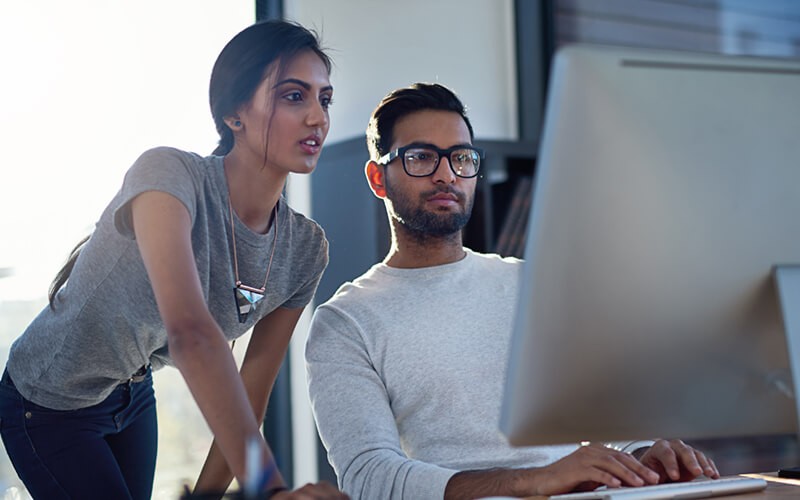 Two business colleagues around desktop computer in open office