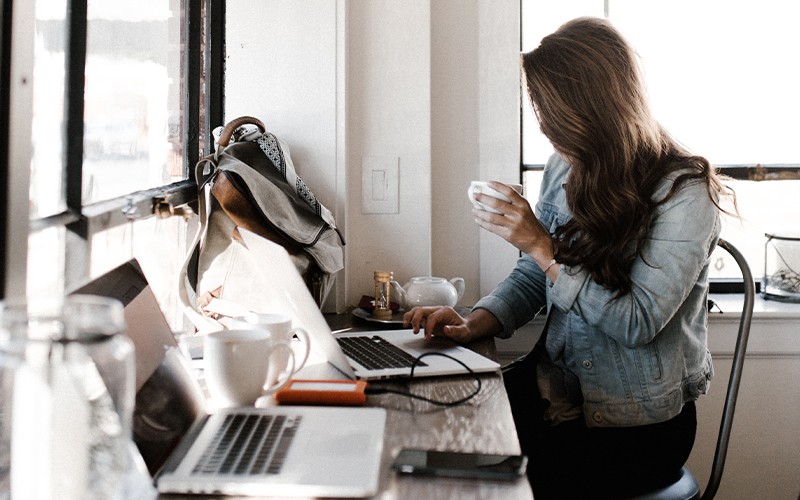Elevate your device management approach. Woman working on laptop at coffee shop