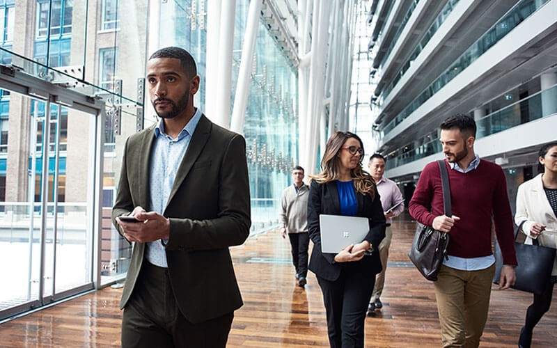 Enterprise Mobility + Security (EMS) Business professionals walking through building with Microsoft devices