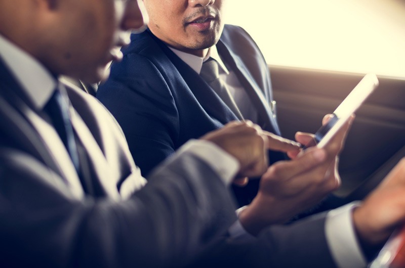 Run apps anywhere, anytime Two business men in a car looking at smart phone.