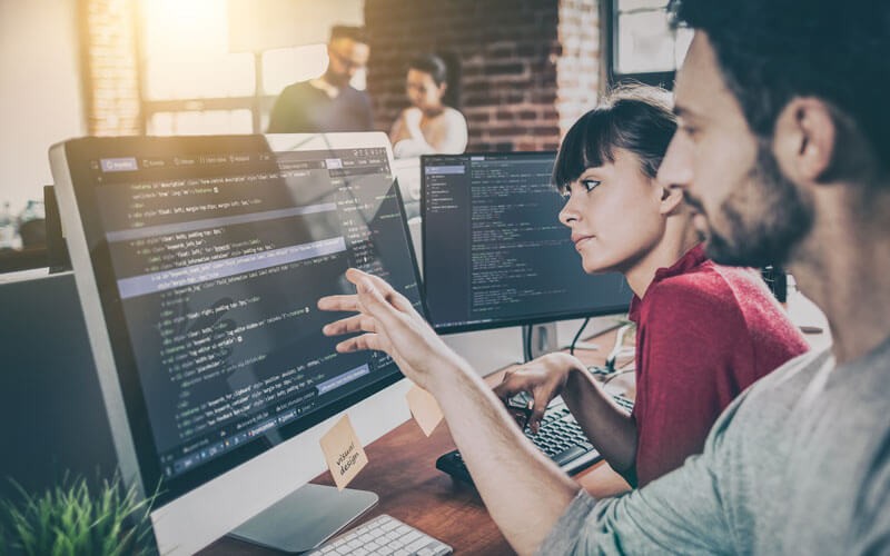 Two developers review code and data on desktop computers
