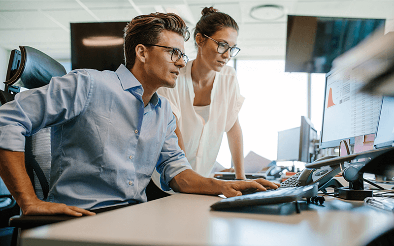 Two IT professionals reading report on desktop computer