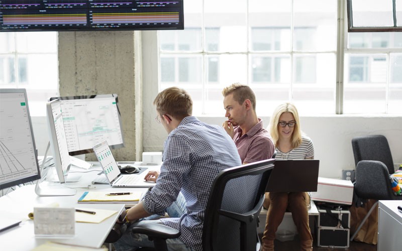 Coworkers collaborating in open office using desktop and laptop devices