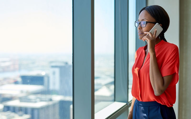 Transform any organization Woman looking out building window holding mobile phone