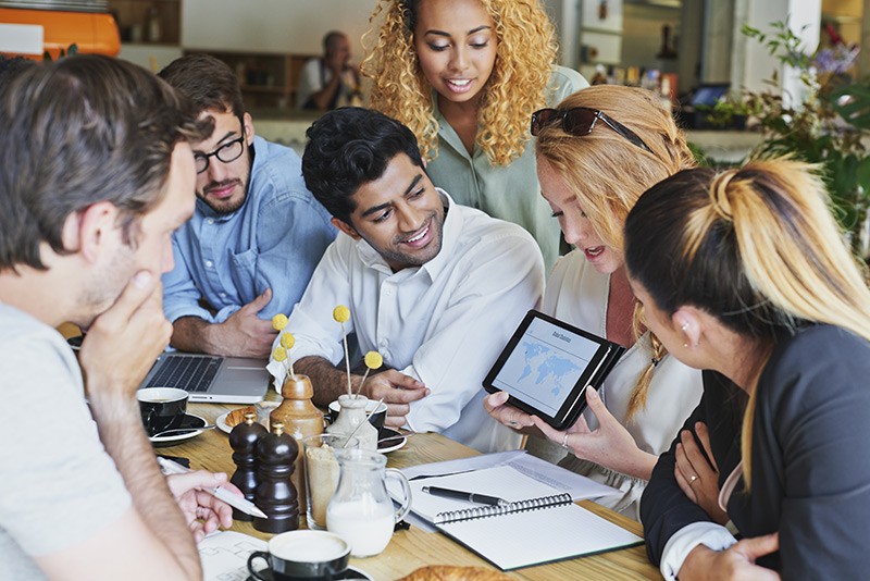 Work from anywhere on any device Team meets in a cafe to discuss project using multiple mobile devices