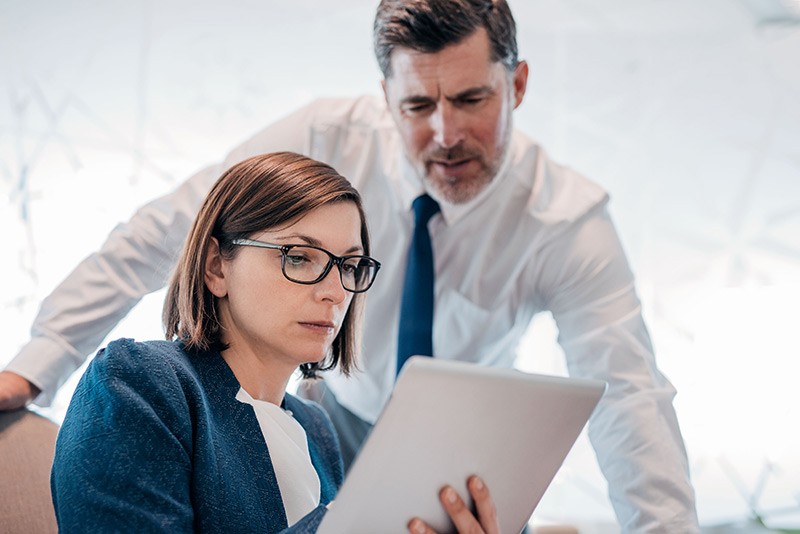 Manager looks over employees shoulder to assist in project development