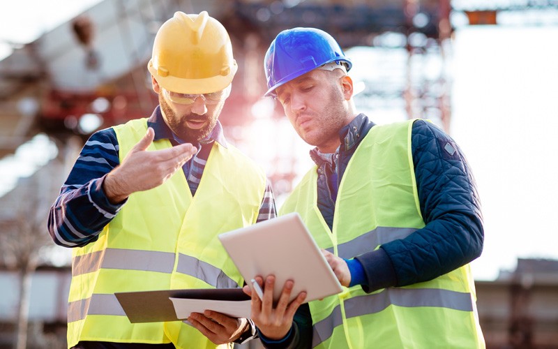 Turn ideas into positive business outcomes Construction workers in hard hats on site using tablet device