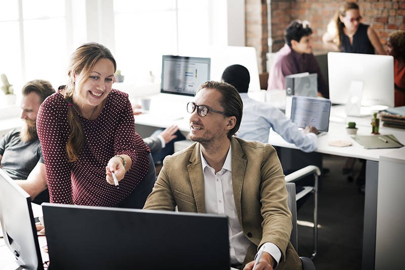 Save more, focus on your business and achieve peace of mind Business manager speaking with employee at desktop computer while team works behind them