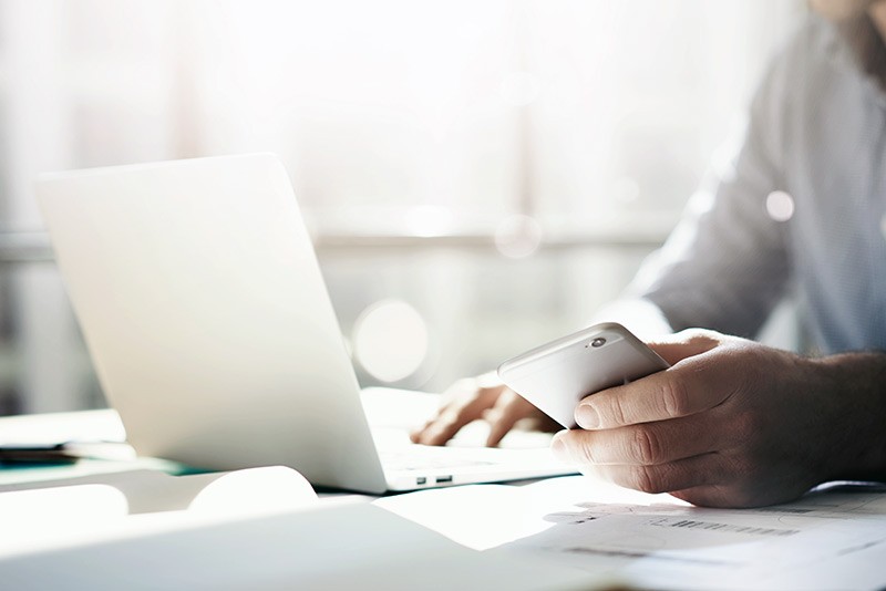 Centralize and properly maintain assets Business professional using smart phone while at notebook computer
