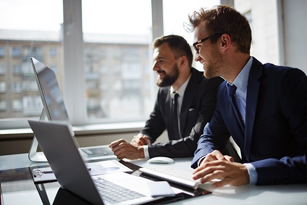 An assigned project manager to coordinate your integration Two smiling businessmen look over desktop computers